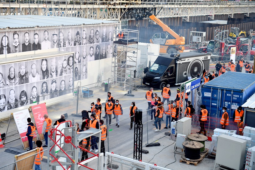 Mur de portraits en noir et blanc et camion « Inside Out » de l’artiste JR sur le chantier