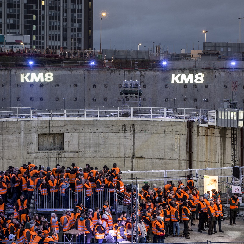 Le public en gilet orange de chantier autour du puits des croisements des tunneliers des lignes 15 sud et 14 sud, mis en lumière dans le cadre du KM8
