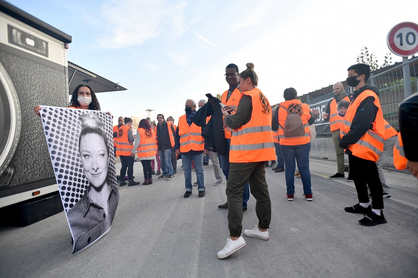 Des participants au KM en gilet orange de chantier se font tirer le portrait devant le camion « Inside Out » de l’artiste JR 