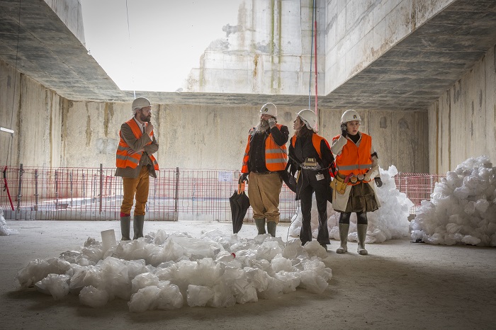 Quatre comédiens en gilets de chantier orange sous le puits d’un chantier du Grand Paris Express dans le cadre du spectacle théâtralisé « Visite insolite de chantier » par la Compagnie Méliadès dans le chantier de l’entonnement Salengro à Champigny-sur-Marne en 2021