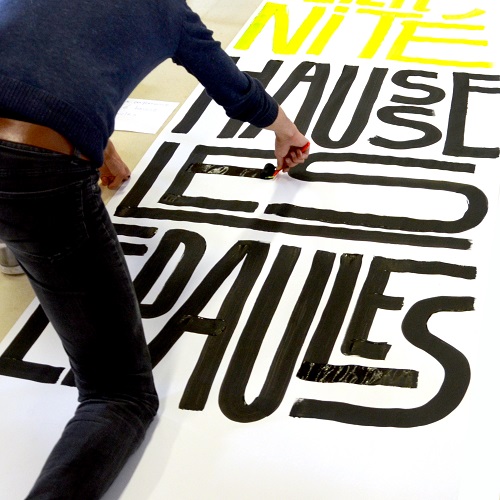 Le designer Eddy Terki en train de peindre des lettres sur un support blanc à la peinture noire 