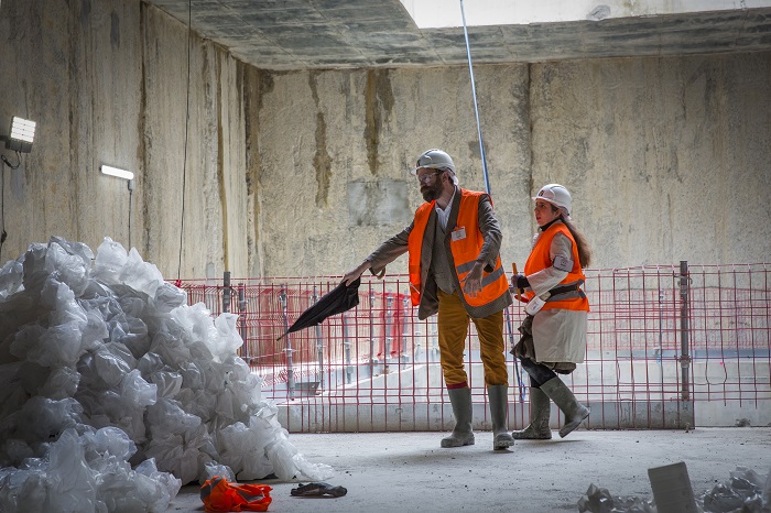 Deux comédiens en gilets de chantier orange sous le puits d’un chantier du Grand Paris Express dans le cadre du spectacle théâtralisé « Visite insolite de chantier » par la Compagnie Méliadès dans le chantier de l’entonnement Salengro à Champigny-sur-Marne en 2021
