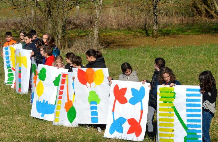 Une ligne d’enfants tiennent des affiches colorées avec des motifs graphiques, dans un espace vert et naturel 