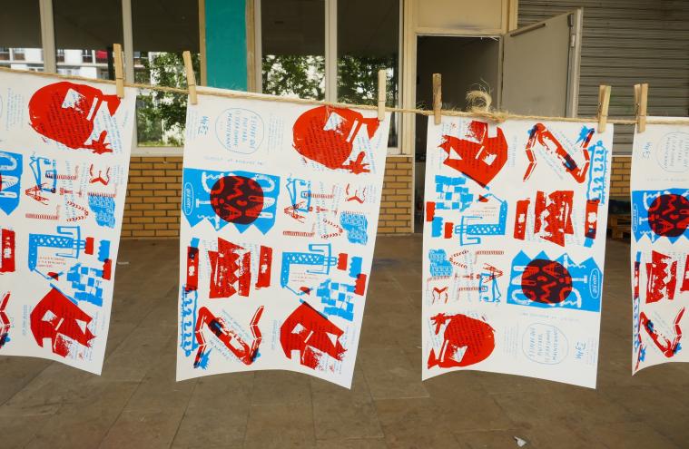 Quatre livrets avec des motifs graphiques bleus et rouges, suspendus à une corde avec des pinces dans le cadre du projet « Ligne Z », chantier partagé du collectif « Ne Rougissez Pas » autour de la gare de Vitry-Centre