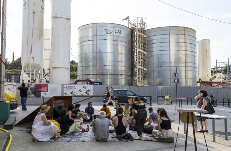 Un groupe de participants assis devant les palissades du chantier d’Arcueil-Cachan dans le cadre de la restitution du chantier partagé avec Yes We Camp