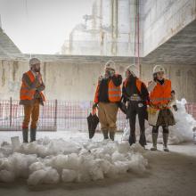 Quatre comédiens en gilets de chantier orange sous le puits d’un chantier du Grand Paris Express dans le cadre du spectacle théâtralisé « Visite insolite de chantier » par la Compagnie Méliadès dans le chantier de l’entonnement Salengro à Champigny-sur-Marne en 2021