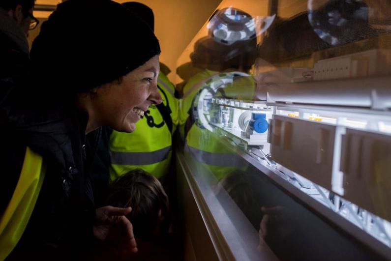 Le public en gilet jaune de chantier observe une maquette de tunnelier du Grand Paris Express sous verre 