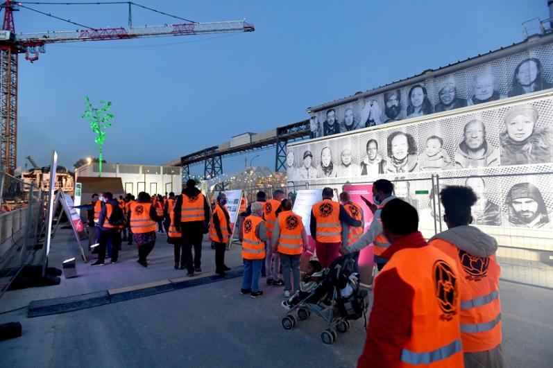 Des participants au KM en gilet orange de chantier se font tirer le portrait devant le camion « Inside Out » de l’artiste JR 