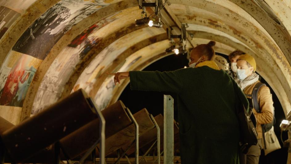 Une personne regarde une exposition photographique dans un espace en forme de tunnel, dans le cadre d’une exposition de la Compagnie Tangible à Vitry-sur-Seine