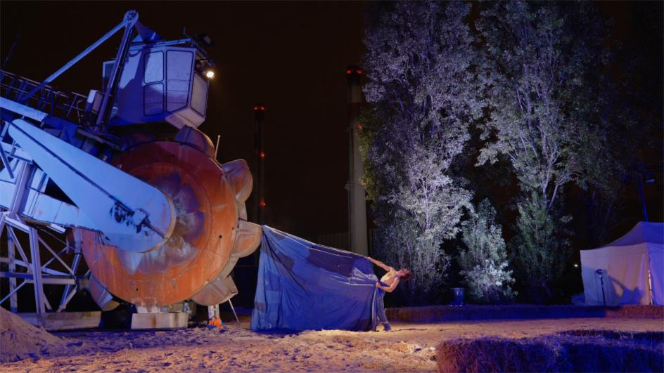 Un engin de chantier avec une roue de grande taille et un danseur avec un grand tissu, dans le cadre du projet de la Compagnie Tangible à Vitry-sur-Seine