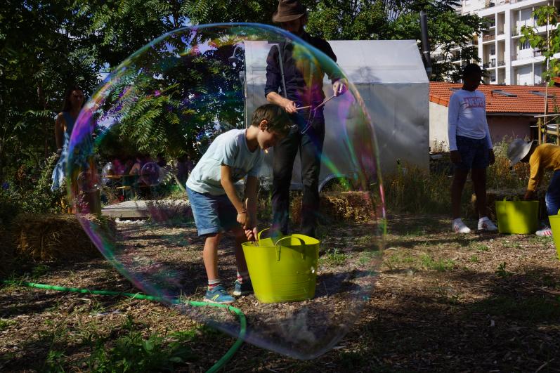 enfant en train de jardiner derrière une bulle de savon